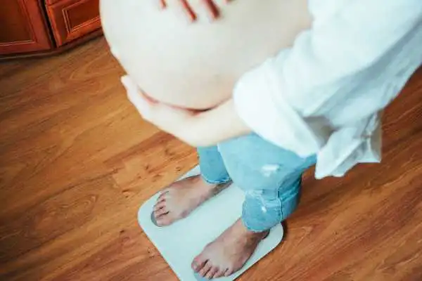 Image of woman weighing herself and experiencing weight gain through pregnancy Amesbury